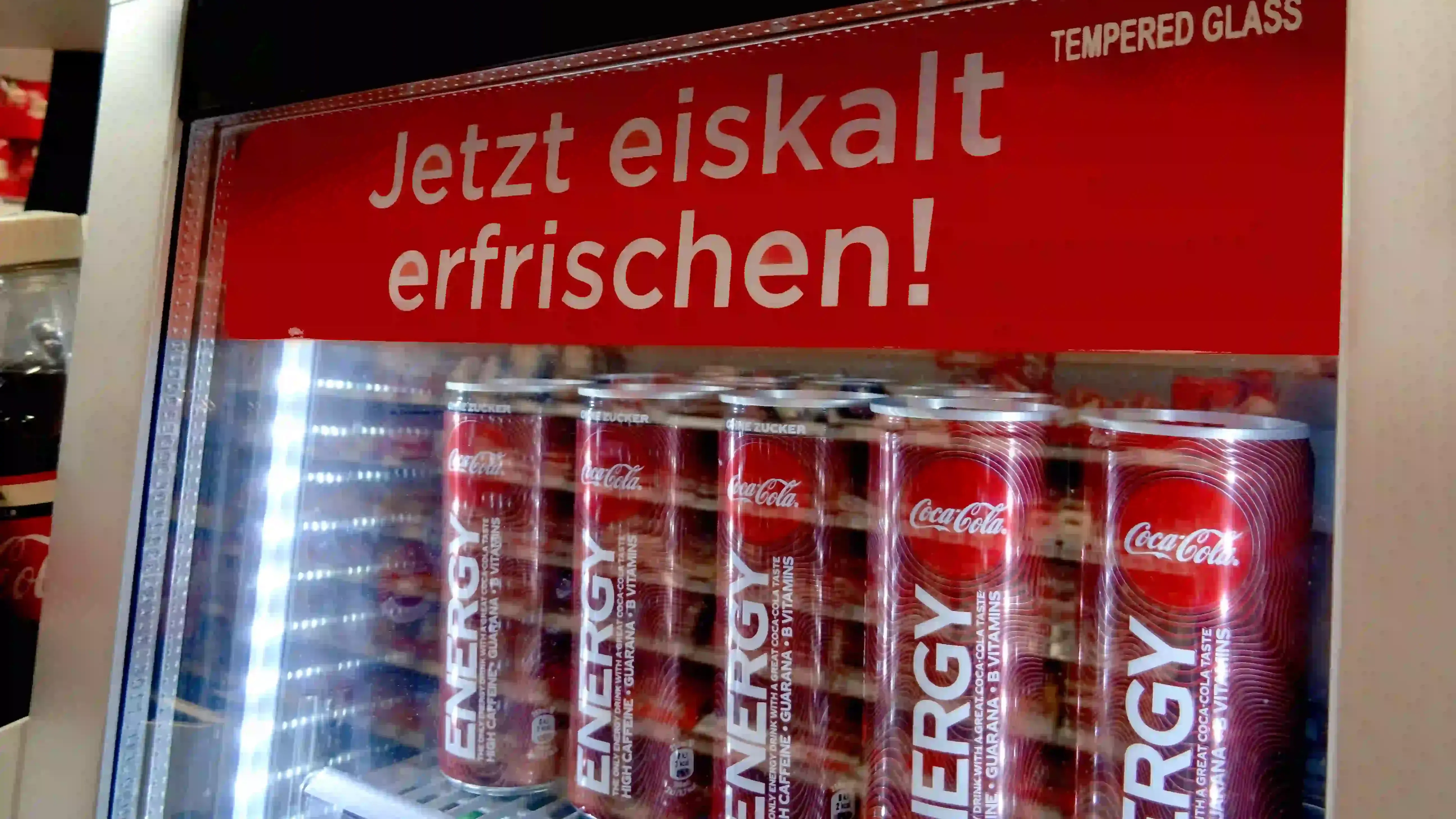 Cans stacked in a refrigerator display, illuminated by bright interior lights