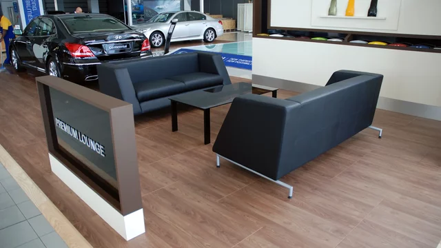 Couches arranged in showroom lounge beside luxury cars on wooden flooring