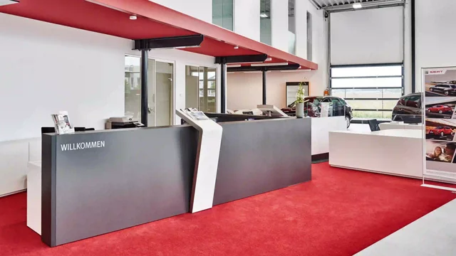 Reception desk stands in modern showroom with cars and red carpet