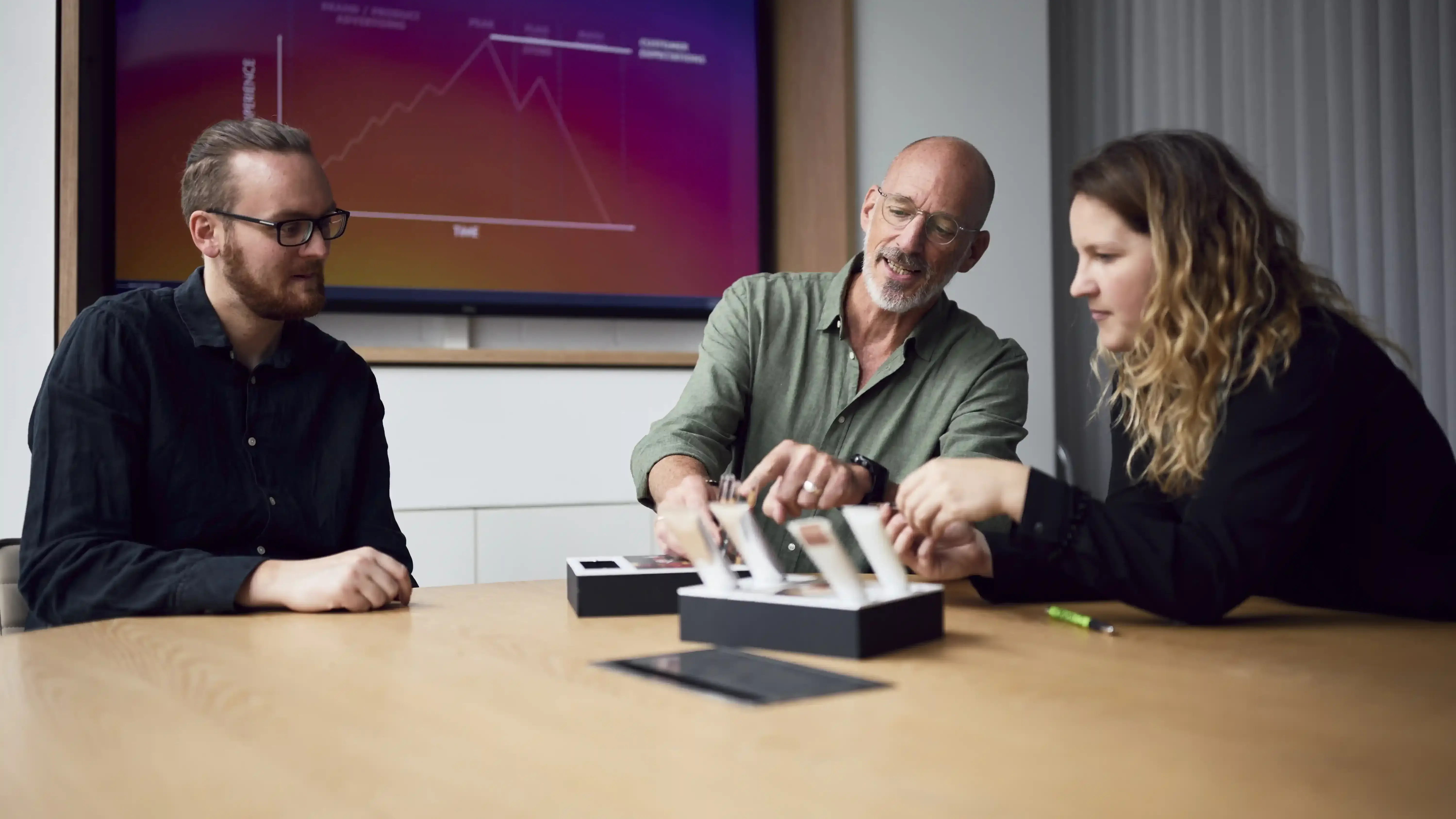 Three people discuss product samples at a table in a meeting room